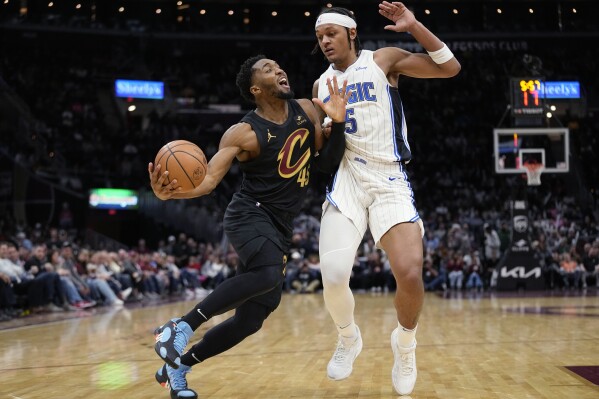Cleveland Cavaliers guard Donovan Mitchell, left, drives around Orlando Magic forward Paolo Banchero during the second half of an NBA basketball game Wednesday, Dec. 6, 2023, in Cleveland. (APPhoto/Sue Ogrocki)
