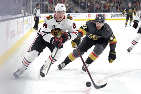 Chicago Blackhawks center Sam Lafferty (24) and Vegas Golden Knights defenseman Shea Theodore (27) skate after the puck during the first period of an NHL hockey game Saturday, March 26, 2022, in Las Vegas. (AP Photo/David Becker)