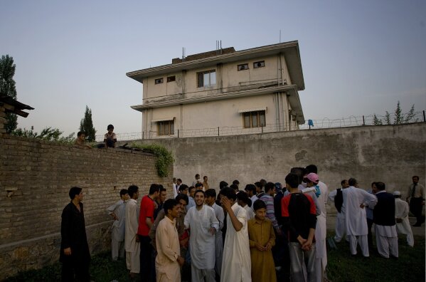 
              FILE - In this May 3, 2011 file photo, local residents gather outside a house where al-Qaida leader Osama bin Laden was killed in Abbottabad, Pakistan. Years after the death of his father at the hands of a U.S. Navy SEAL raid in Pakistan, Hamza bin Laden himself clearly in the crosshairs of world powers. The U.S. has put up to a $1 million bounty for him. The U.N. Security Council has named him to a global sanctions list, sparking a new Interpol notice for his arrest. His home country of Saudi Arabia has revoked his citizenship. (AP Photo/B.K.Bangash,File)
            