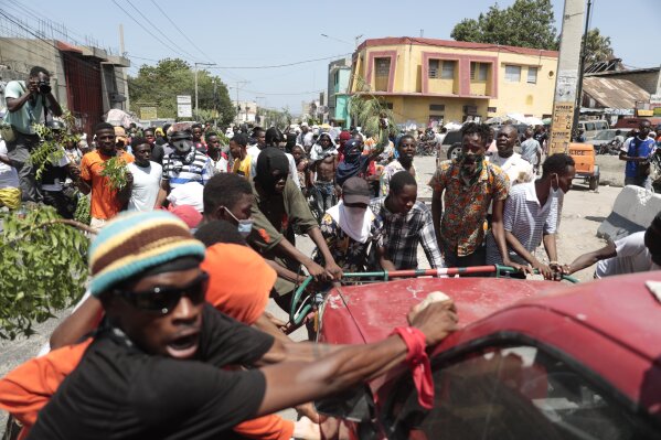 Protesters try to flip a car to block a street during a protest against insecurity in Port-au-Prince, Haiti, Monday, Aug. 7, 2023. (AP Photo/Odelyn Joseph)