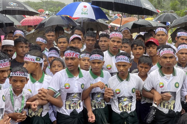 Rohingya refugees gather in the rain to demand safe return to Myanmar's Rakhine state as they mark the seventh anniversary of their mass exodus at their refugee camp at Kutupalong in Cox's Bazar district, Bangladesh, Sunday, Aug. 25, 2024. (AP Photo/ Shafiqur Rahman)
