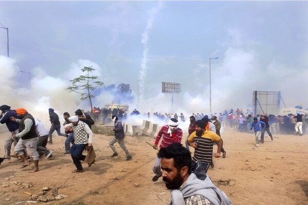 Farmers run for cover after police fired tear gas to disperse protesting farmers who were marching to New Delhi near the Punjab-Haryana border at Shambhu, India, Tuesday, Feb.13, 2024. Farmers are marching to the Indian capital asking for a guaranteed minimum support price for all farm produce. (APPhoto/Rajesh Sachar)