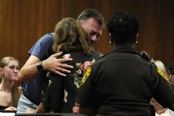Buck Myre, background, father of slain Oxford student Tate Myre, hugs Assistant Principal Kristy Gibson-Marshall in court, Friday, July 28, 2023, in Pontiac, Mich. Prosecutors are making their case that the Michigan teenager should be sentenced to life in prison for killing four students at his high school in 2021. Prosecutors introduced dark journal entries written by Ethan Crumbley, plus chilling video and testimony from a wounded staff member. (AP Photo/Carlos Osorio)
