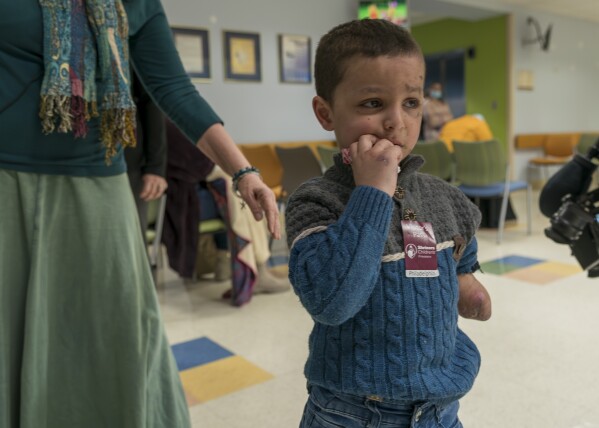 Four-year-old Omar Abu Kuwaik, from Gaza, stands in a waiting room at Shriners Children's Hospital, Thursday, Jan. 18, 2024, in Philadelphia. On Dec. 6, 2023 two Israeli airstrikes slammed into Omar's grandparents' home in the Nuseirat refugee camp, in central Gaza. The explosion peeled the skin from his face, exposing raw pink layers peppered with deep lacerations. His left arm could not be saved below the elbow. His parents, 6-year-old sister, grandparents, two aunts and a cousin were killed. (AP Photo/Peter K. Afriyie)