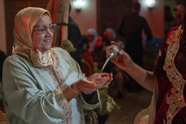 A woman sprinkle orange blossom water after it was distilled, in a cultural center in Marrakech, Morocco, Saturday, March 23, 2024. Moroccan cities are heralding in this year's spring with orange blossoms by distilling them using traditional methods. Orange blossom water is mostly used in Moroccan pastries or mint tea and sprinkled over heads and hands in religious ceremonies. (AP Photo)