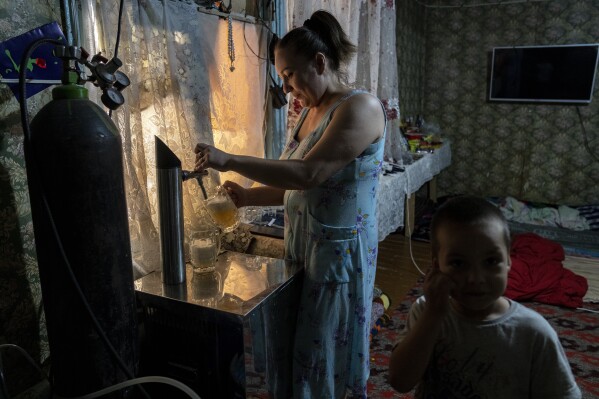 A woman serves beer to customers in her house, which she uses as a shop, in a village far outside of Muynak, Uzbekistan, Saturday, June 24, 2023. (AP Photo/Ebrahim Noroozi)