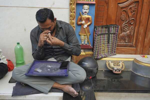 A trader inspects a diamond as he sits on a pavement at a market in Surat, India, on April 14, 2025. (AP Photo/Ajit Solanki)