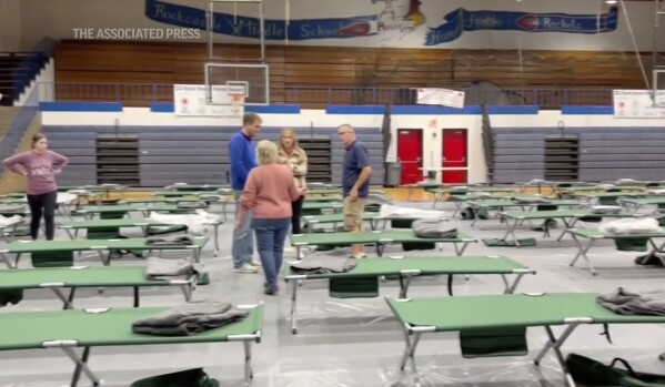 This image taken from video and provided by WTVQ shows people helping arrange cots at Rockcastle Middle School, being used as an evacuation center, in Mt Vernon, Ky., Wednesday, Nov. 22, 2023. People were evacuated from a nearby town after a CSX train derailed Wednesday near Livingston, a remote town with about 200 people in Rockcastle County. CSX says two of the 16 cars that derailed carried molten sulfur, which caught fire after the cars were breached. (WTVQ via AP)