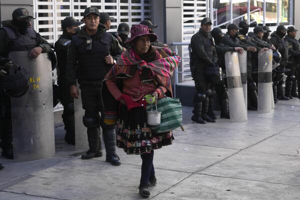 A woman walks past police officers standing guard the Financial Regulatory Authority offices, in La Paz, Bolivia, Wednesday, May 31, 2023. A prosecutor in Bolivia launched an investigation Monday into the mysterious death of the trustee of a bankrupt bank who fell from the 15th floor of a building and his family disputed claims he took his own life. (AP Photo/Juan Karita).