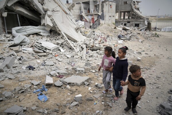 Children walk by the destroyed house of journalist Islam Meqdad, where she was killed along with her son and five other family members in an Israeli army strike in Khan Younis, southern Gaza Strip, Sunday, April 6, 2025. (AP Photo/Abdel Kareem Hana)