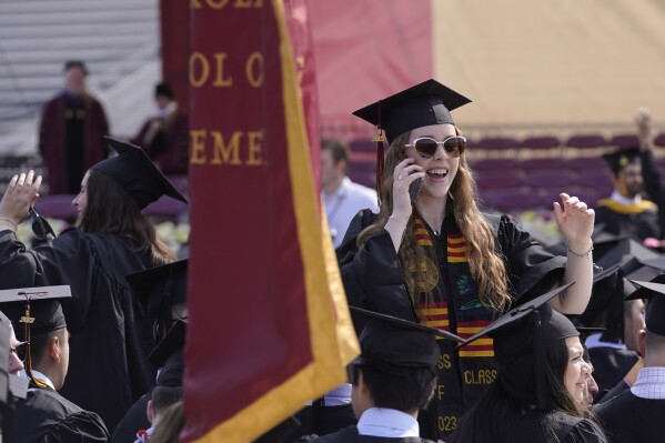 File - A graduating Boston College student speaks on a phone during commencement ceremonies on May 22, 2023, in Boston. The Free Application for Federal Student Aid, or FAFSA, has been available on and off for a few days now. While many have been able to take advantage of the new shorter application, many others have struggled to even open the application. (AP Photo/Steven Senne, File)