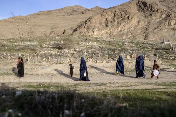 Women walk through a cemetery in a village in a remote region of Afghanistan, on Friday, Feb. 24, 2023. A farmer, his wife and their five children killed during a Sept. 5, 2019, night raid by U.S. forces, were buried here, where generations of their kin had been laid to rest. (AP Photo/Ebrahim Noroozi)