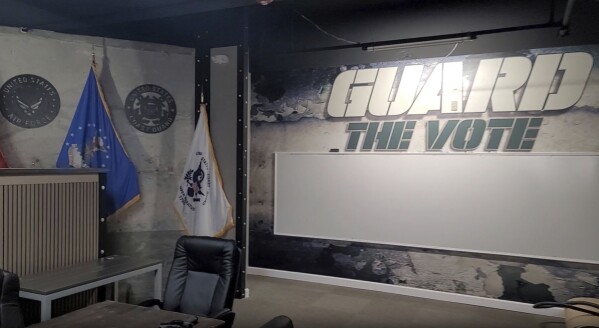 This screenshot of an undated video provided by Victor Mailer shows the inside details of what Mailer says "command center" In Venice, Florida for his group, Guard the Vote.  The image shows the group's name, military flags, and Mellor's handgun on a table.  (Victor Mailer via AP)