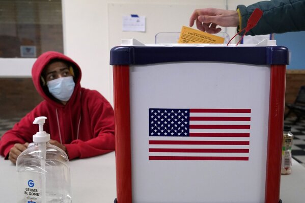Election inspector Taquaine Mason observes as a voter drops his ballot into the box during early in-person voting, Thursday, Oct. 29, 2020, in Cambridge, Mass. (AP Photo/Elise Amendola)