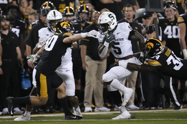 Michigan State running back Nathan Carter (5) runs between Iowa defensive back Quinn Schulte (30) and linebacker Jay Higgins (34) during the first half of an NCAA college football game, Saturday, Sept. 30, 2023, in Iowa City, Iowa. (AP Photo/Charlie Neibergall)