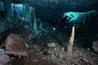 This Dec. 12, 2019 photo released by CINDAQ.ORG, or "Centro Investigador del Sistema Acuífero de Quintana Roo," shows a diver in the "La Mina Roja" passage of the Sagitario underwater cave system near Playa del Carmen in Mexico's Yucatan Peninsula. The discovery of remains of human-set fires, stacked mining debris, simple stone tools, navigational aids, and digging sites suggest humans went into the caves around 12,000 to 14,000 years ago, seeking iron-rich red ocher, which early peoples in the Americas prized for decoration and rituals. (CINDAQ.ORG via AP)