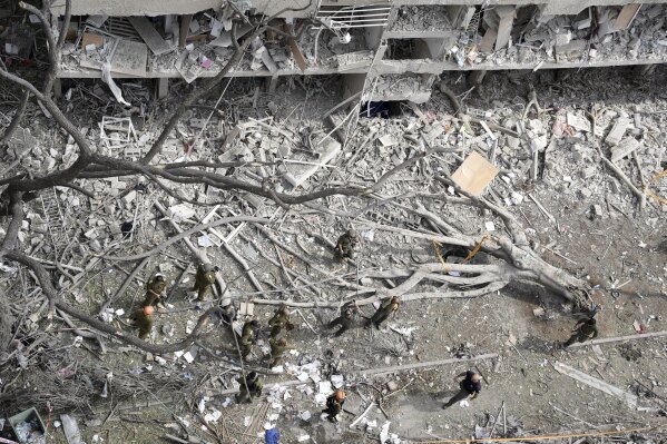 A torn-out tree lies among the rubble as firefighters, rescue workers, and military personnel survey the site of a direct missile strike launched from Iran in Tel Aviv, Israel, Sunday, June 22, 2025. (AP Photo/Oded Balilty)