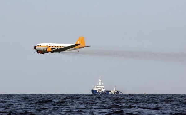 FILE - A plane drops chemicals to help disperse oil from a leaking pipeline that resulted from an explosion and collapse of the Deepwater Horizon oil rig in the Gulf of Mexico near the coast of Louisiana, April 27, 2010. When a deadly explosion destroyed BP's Deepwater Horizon drilling rig in the Gulf of Mexico, tens of thousands of ordinary people were hired to help clean up the environmental devastation. These workers were exposed to crude oil and the chemical dispersant Corexit while picking up tar balls along the shoreline, laying booms from fishing boats to soak up slicks and rescuing oil-covered birds. (AP Photo/Patrick Semansky, File)