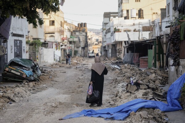 A Palestinian woman walks on a damaged road in the Jenin refugee camp in the West Bank, Wednesday, July 5, 2023, after the Israeli army withdrew its forces from the militant stronghold. The withdrawal of troops from the camp ended an intense two-day operation that killed at least 13 Palestinians, drove thousands of people from their homes and left a wide swath of damage in its wake. One Israeli soldier was also killed. (AP Photo/Majdi Mohammed)