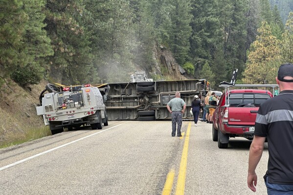 This image provided by Samantha Grange shows people looking on at the scene of an overturned school bus along Highway 55, Friday, Aug. 4, 2023, about 60 miles north of Boise, Idaho. The school bus carrying teenage campers rolled over on a winding Idaho highway Friday afternoon, injuring 11 people, the Idaho State Police said. (Samantha Grange via AP)