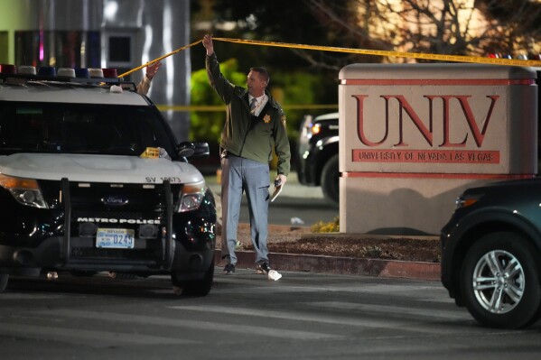 A police officer walks under crime scene tape after a shooting at the University of Nevada, Las Vegas, on Wednesday, Dec. 6, 2023.  (AP Photo/John Locher)