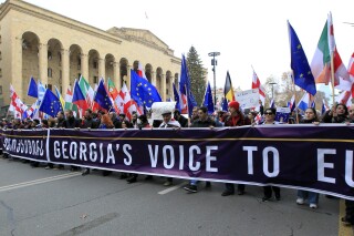 Demonstrators carry EU and Georgian flags during a march in support of Georgia's EU candidacy with the building of Georgian Parliament in the left, in Tbilisi, Georgia, Dec. 9, 2023. (AP Photo/Shakh Aivazov)
