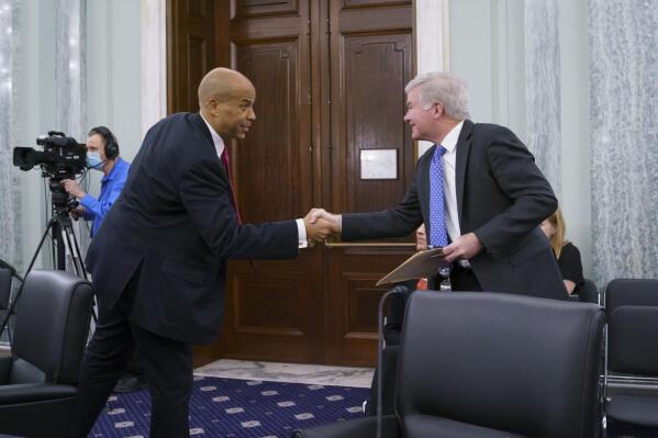 Sen. Cory Booker, D-N.J., left, greets NCAA President Mark Emmert, as the Senate Commerce, Science, and Transportation Committee holds a hearing on student athlete compensation and federal legislative proposals to enable athletes participating in collegiate sports to monetize their name, image, and likeness, at the Capitol in Washington, Wednesday, June 9, 2021. (AP Photo/J. Scott Applewhite)