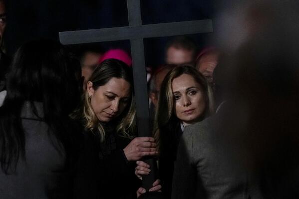 Two nurses, Albina from Russia, right, and Irina, from Ukraine hold the cross as they take part in the Via Crucis (Way of the Cross) torchlight procession presided by Pope Francis on Good Friday in front of Rome's Colosseum, in Rome, Friday, April 15, 2022. (AP Photo/Gregorio Borgia)