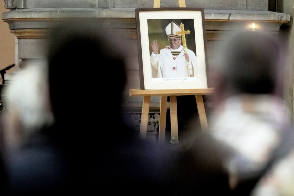 Believers sit in front of a photo of the late Pope Francis after the news of his death, during a Easter service at the Basilica of St. John the Baptist, near the Vatican embassy, in Berlin, Germany, Monday, April 21, 2025. (AP Photo/Markus Schreiber)