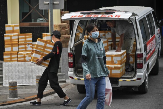 A woman wearing a face mask walks by workers loading off stocks from a van outside a commercial office building in Beijing, Tuesday, Aug. 8, 2023. China's exports plunged by 14.5% in July compared with a year earlier, adding to pressure on the ruling Communist Party to reverse an economic slump. (AP Photo/Andy Wong)