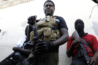 Barbecue, the leader of the "G9 and Family" gang, stands with his fellow gang members after speaking to journalists in the Delmas 6 neighborhood of Port-au-Prince in Port-au-Prince, Haiti, Tuesday, March 5, 2024. Haiti's latest violence began with a direct challenge from the former elite police officer Jimmy Chérizier, known as Barbecue, who said he would target government ministers to prevent the prime minister's return and force his resignation. (AP Photo/Odelyn Joseph)