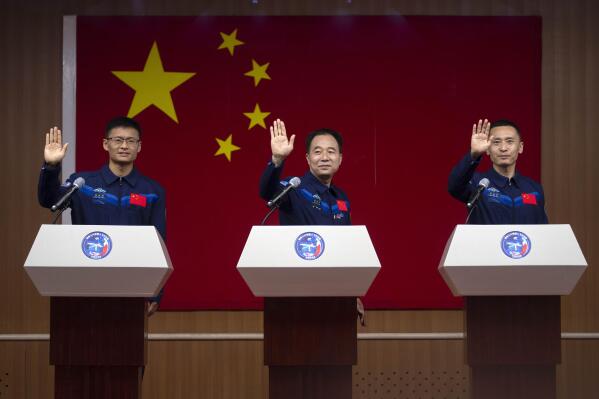 Chinese astronauts for the upcoming Shenzhou-16 mission, from left, Gui Haichao, Jing Haipeng, and Zhu Yangzhu wave as they stand behind glass during a meeting with the press at the Jiuquan Satellite Launch Center in northwest China on Monday, May 29, 2023. China's space program plans to land astronauts on the moon before 2030, a top official with the country's space program said Monday. (AP Photo/Mark Schiefelbein)