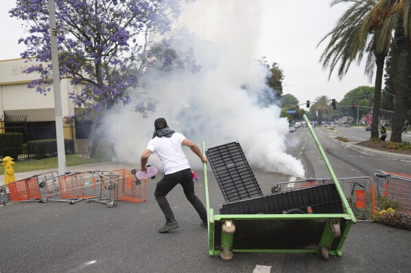 A protester looks on as Border Patrol personnel in riot gear and gas masks stood guard outside an industrial park in the Paramount section of Los Angeles, Saturday, June 7, 2025. (AP Photo/Eric Thayer)