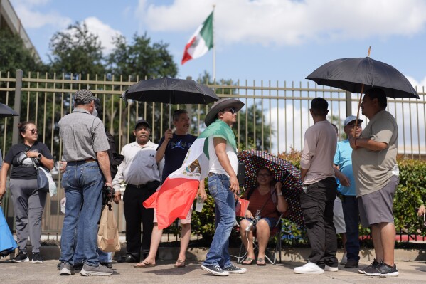 Max Aleman, center, wears a Mexican flag as he waits for hours along with others to vote in the Mexican election at the Mexican Consulate building Sunday, June 2, 2024, in Houston. Houston and Dallas were the only two consulate locations in Texas where Mexican nationals could go to vote. Mexicans went to the polls Sunday to vote for who will likely be the country's first female president. (AP Photo/David J. Phillip)
