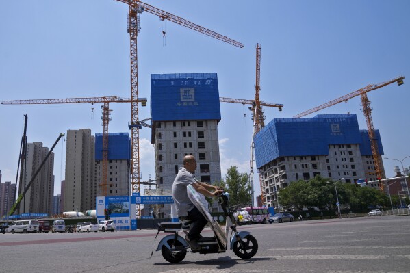 FILE - A man rides on an electric bike past by a residential buildings under construction in Beijing on June 5, 2023. Chinese factory activity contracted in July as export orders shrank, a survey showed Monday, adding to pressure on the ruling Communist Party to reverse an economic slowdown. (AP Photo/Andy Wong, File)