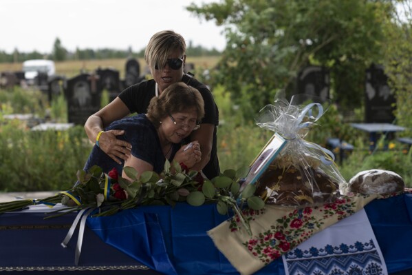 Comforted by Khrystyna Liubymska, top, Zynaida Nedoleshko weeps next to a casket carrying the remains of her nephew, Roman Shadlovskyi, during a reburial service for him in Bucha, Ukraine, Tuesday, July 18, 2023. The Ukrainian armed forces veteran, who was initially buried in a mass grave as an unidentified victim after being killed last year by Russian troops, received a reburial Tuesday after a DNA test confirmed his identity. (AP Photo/Jae C. Hong)