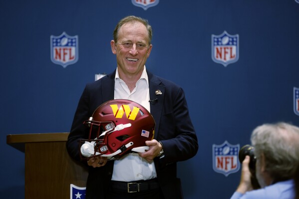 Josh Harris, leader of a group buying the Washington Commanders, poses with a team helmet after NFL owners voted to approve the sale in Bloomington, Minn., Thursday, July 20, 2023. (AP Photo/Bruce Kluckhohn)