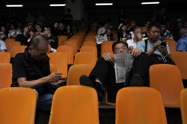 A visitor reads a horse racing paper at the Macao Jockey Club in Macao, Saturday, March 30, 2024. After more than 40 years, Macao’s horse racing track hosted its final races on Saturday, bringing an end to the sport in the city famous for its massive casinos. (AP Photo/Louise Delmotte)