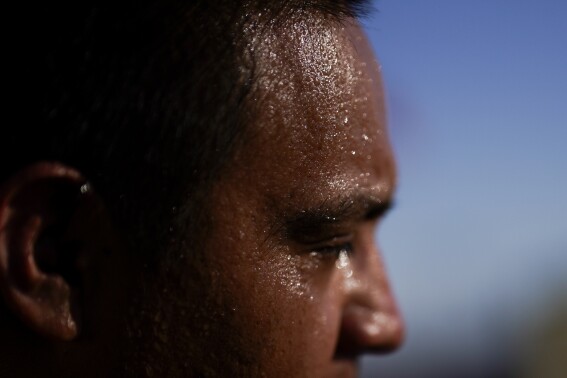 FILE - Sweat covers the face of Juan Carlos Biseno after dancing to music from his headphones as afternoon temperatures reach 115 degrees Fahrenheit (46.1 Celsius), July 19, 2023, in Calexico, Calif. More Americans believe they've personally felt the impact of climate change because of recent extreme weather, including a summer that brought dangerous heat for much of the United States, according to new polling from The Associated Press-NORC Center for Public Affairs Research. (AP Photo/Gregory Bull, File)