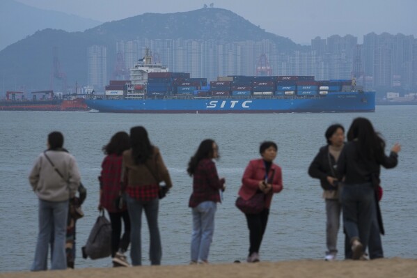 Tourists enjoy sea scenery as a containers vessel sails by residential buildings in Xiamen in southeast China's Fujian province on Dec. 26, 2023. China's efforts to restore confidence and rev up the economy will top the agenda during this month’s meeting of the ceremonial national legislature. (AP Photo/Andy Wong)