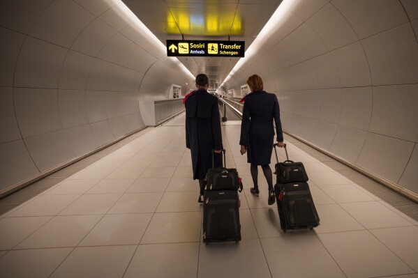 Flight attendants arriving at the Henri Coanda International Airport pass under a Schengen Information sign, in Otopeni, near Bucharest, Romania, Sunday, March 31, 2024. Romania and Bulgaria joined Europe's passport- and visa-free Schengen Area, applying only to travelers arriving by air and sea. (AP Photo/Andreea Alexandru)