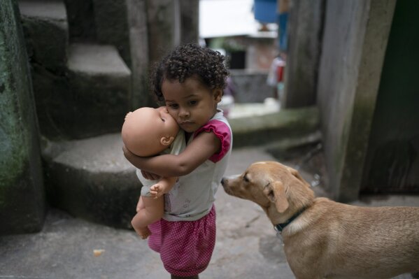 A girl holds her doll in an alley of the Rocinha slum of Rio de Janeiro, Brazil, Tuesday, March 24, 2020. The narrow alleyways of Brazil's largest favela reduce airflow around homes packed tightly together and the poor neighborhood, which lacks proper sewage, has a high incidence of tuberculosis. Authorities are concerned that COVID-19 could easily spread in the favelas of Rio. (AP Photo/Leo Correa)
