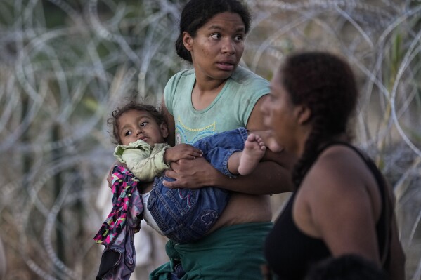 FILE - A woman carries her child after she and other migrants crossed the Rio Grande and entered the U.S. from Mexico, to be processed by U.S. Customs and Border Protection, on Sept. 23, 2023, in Eagle Pass, Texas. President Joe Biden has ordered a halt to asylum processing at the U.S. border with Mexico when arrests for illegal entry top 2,500 a day, which was triggered immediately. (AP Photo/Eric Gay, File)