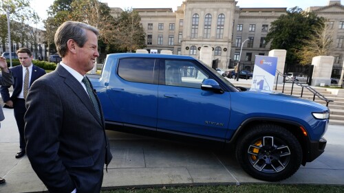 FILE - Gov. Brian Kemp smiles as he stands next to a Rivian electric truck during a ceremony to announce the electric truck maker plans to build a $5 billion battery and assembly plant east of Atlanta that is expected to hires 7,500 workers Thursday, December 16, 2021, in Atlanta. Kemp escalated his attack on President Joe Biden's electric vehicle policy. The Republican governor speaks Tuesday, June 27, 2023, during the groundbreaking for a company that received more than $100 million in federal funding to refine graphite for electric batteries. But Kemp says Biden's infrastructure law misplaces the government's 