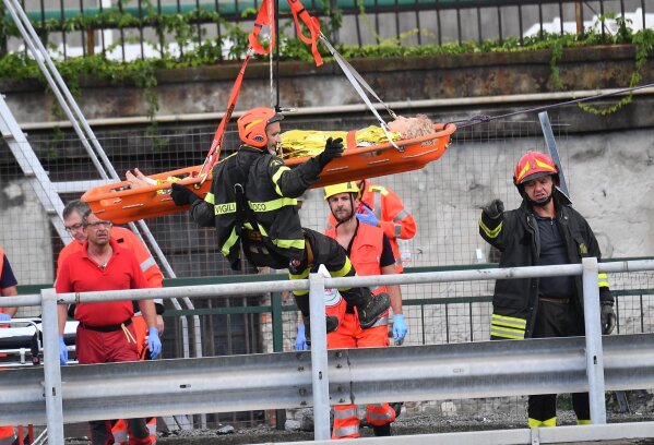 
              Rescuers recover an injured person after the Morandi highway bridge collapsed in Genoa, northern Italy, Tuesday, Aug. 14, 2018. A large section of the bridge collapsed over an industrial area in the Italian city of Genova during a sudden and violent storm, leaving vehicles crushed in rubble below. (Luca Zennaro/ANSA via AP)
            