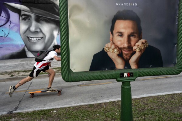 A man skates near an advertising billboard with a portrait of the soccer legend Lionel Messi, in front, and behind a mural with the image of the legendary tango singer Carlos Gardel, in Buenos Aires, Argentina, Monday, Nov. 6, 2023. (AP Photo/Rodrigo Abd)