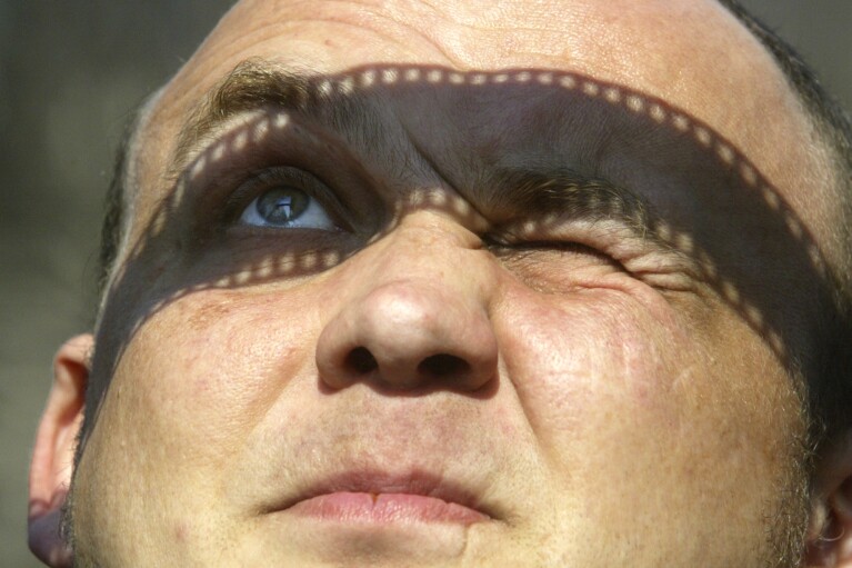 FILE - Ukrainian man watches a partial solar eclipse through a strip of film in Kyiv, Ukraine, Wednesday, March 29, 2006. The moon began blocking out the sun in the morning in Brazil before the path of greatest blockage migrated to Africa, then on to Turkey and up into Mongolia, where it will fade out with the sunset. (AP Photo/Efrem Lukatsky, File)