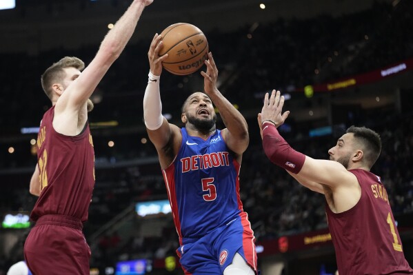 Detroit Pistons guard Monte Morris (5) goes up for a shot between Cleveland Cavaliers forward Dean Wade, left, and guard Max Strus, right, in the second half of an NBA basketball game, Wednesday, Jan. 31, 2024, in Cleveland. (AP Photo/Sue Ogrocki)