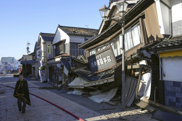 A person walks past a collapsed houses following an earthquake in Wajima, Ishikawa prefecture, Japan Tuesday, Jan. 2, 2024. (Kyodo News via AP)
