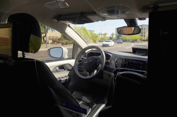 FILE - A Waymo minivan moves along a city street as an empty driver's seat and a moving steering wheel drive passengers during an autonomous vehicle ride, on April 7, 2021, in Chandler, Ariz. The U.S. government's highway safety agency has opened another investigation of automated driving systems, this time into crashes involving Waymo's self-driving vehicles. The National Highway Traffic Safety Administration posted documents detailing the probe on its website early Tuesday after getting 22 reports of Waymo vehicles either crashing or doing something that may have violated traffic laws. (AP Photo/Ross D. Franklin, File)